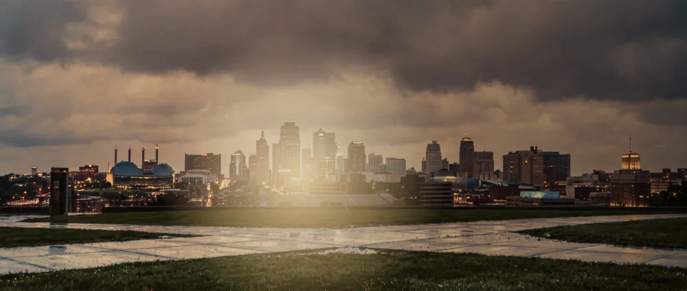 The Kansas City skyline at dusk under heavy cloud, seen across wet open ground.